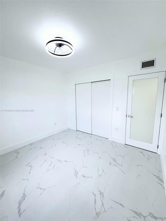 unfurnished bedroom featuring marble finish floor, a closet, visible vents, and baseboards