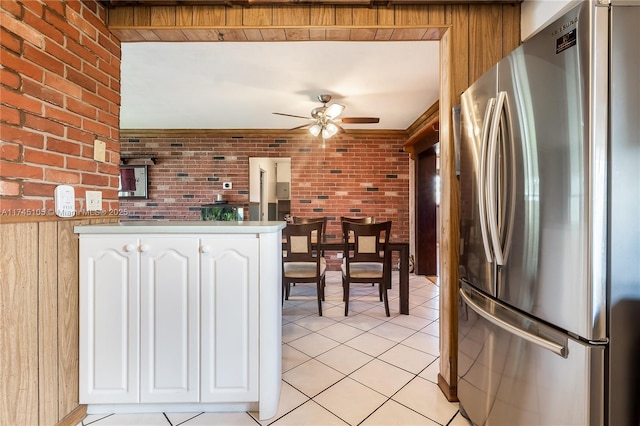 kitchen featuring stainless steel refrigerator, ceiling fan, white cabinetry, brick wall, and light tile patterned flooring