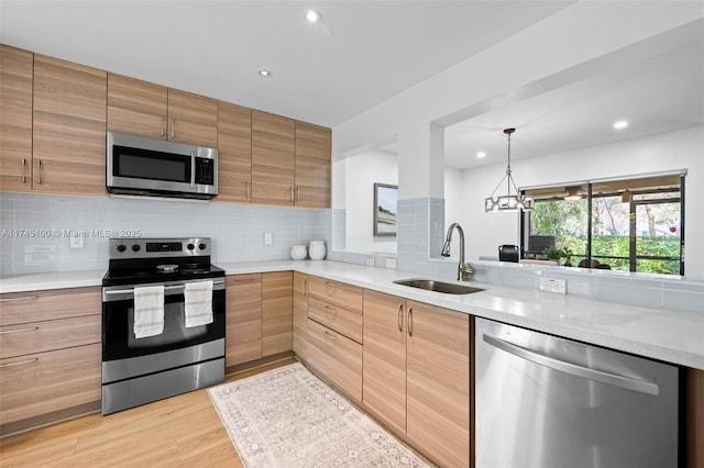 kitchen with sink, backsplash, stainless steel appliances, light hardwood / wood-style floors, and decorative light fixtures