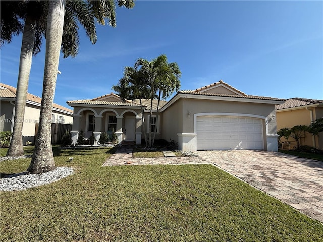 mediterranean / spanish house featuring fence, an attached garage, stucco siding, a front lawn, and decorative driveway