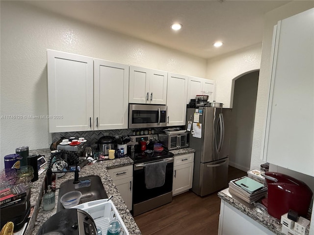 kitchen featuring arched walkways, white cabinets, appliances with stainless steel finishes, and dark wood-style flooring