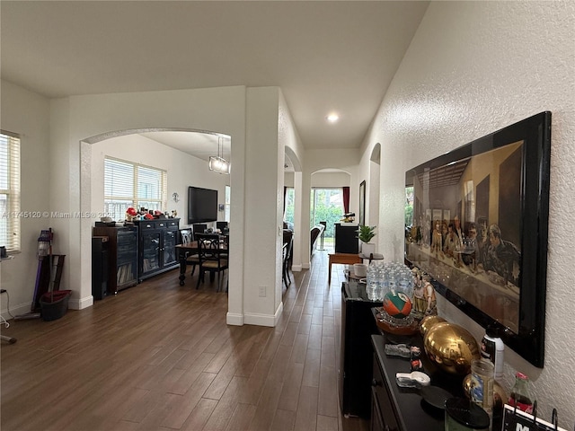 corridor with baseboards, arched walkways, dark wood finished floors, and a textured wall