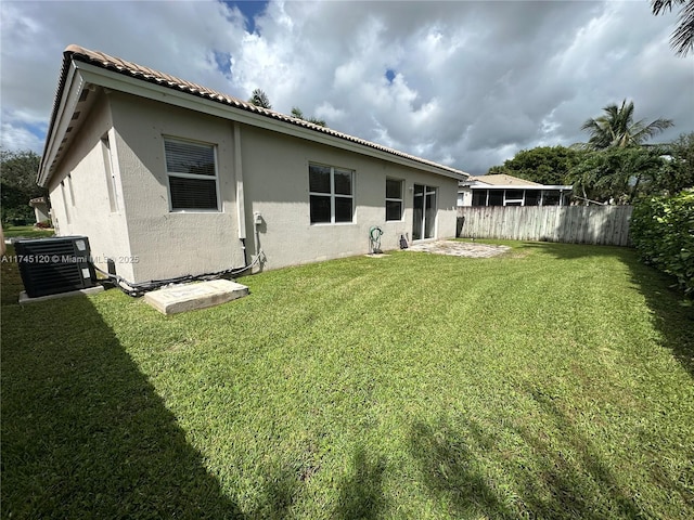 rear view of house featuring fence, stucco siding, central AC unit, a yard, and a patio area