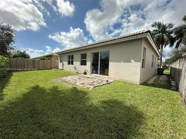 back of house with a tile roof, stucco siding, a yard, a fenced backyard, and a patio area