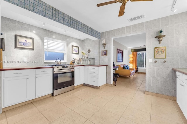 kitchen with tile walls, stainless steel range with gas stovetop, and white cabinets