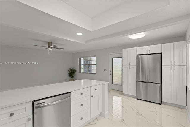 kitchen featuring stainless steel appliances, white cabinets, ceiling fan, and a tray ceiling