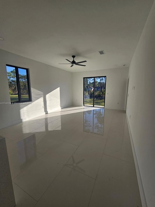 empty room with plenty of natural light, light tile patterned floors, and ceiling fan