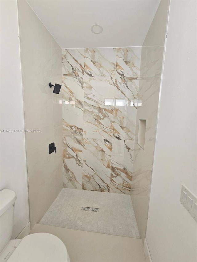 bathroom with a tile shower and toilet