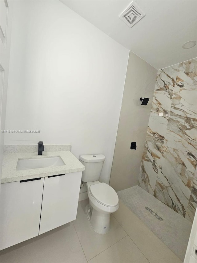 bathroom featuring tile patterned flooring, vanity, a tile shower, and toilet