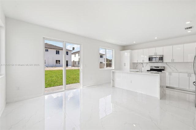 kitchen featuring tasteful backsplash, white cabinetry, sink, stainless steel appliances, and a center island with sink