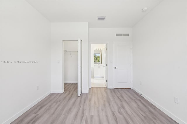 unfurnished bedroom with a spacious closet, light hardwood / wood-style flooring, and a closet