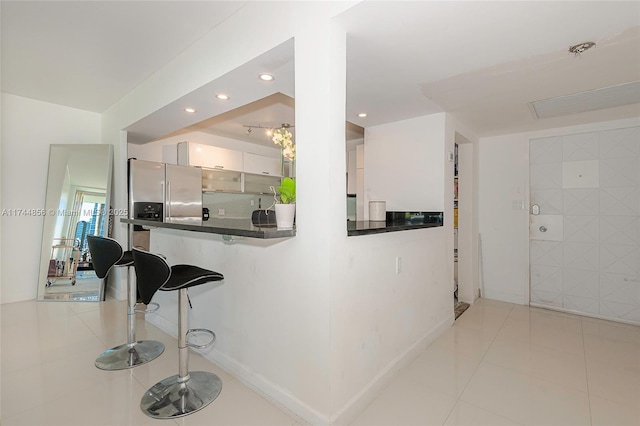 kitchen with light tile patterned flooring, a kitchen bar, white cabinetry, stainless steel fridge with ice dispenser, and kitchen peninsula