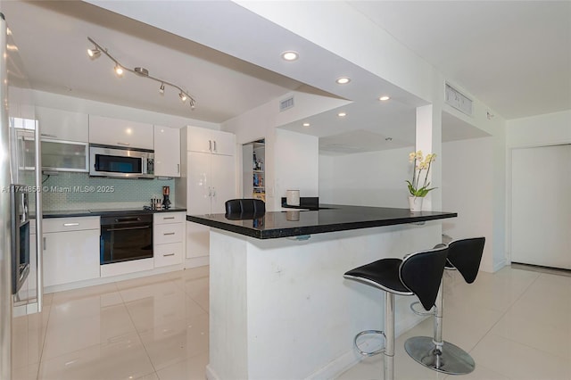 kitchen featuring backsplash, a kitchen breakfast bar, oven, white cabinets, and cooktop