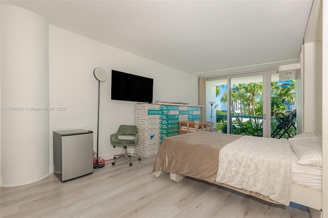 bedroom with access to outside, stainless steel fridge, and light hardwood / wood-style flooring