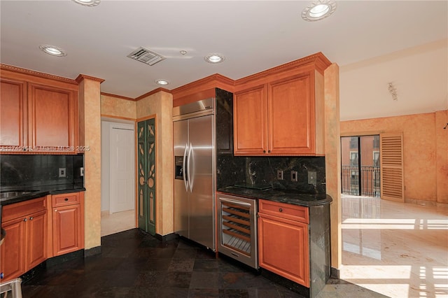 kitchen featuring built in fridge, dark stone counters, beverage cooler, and visible vents