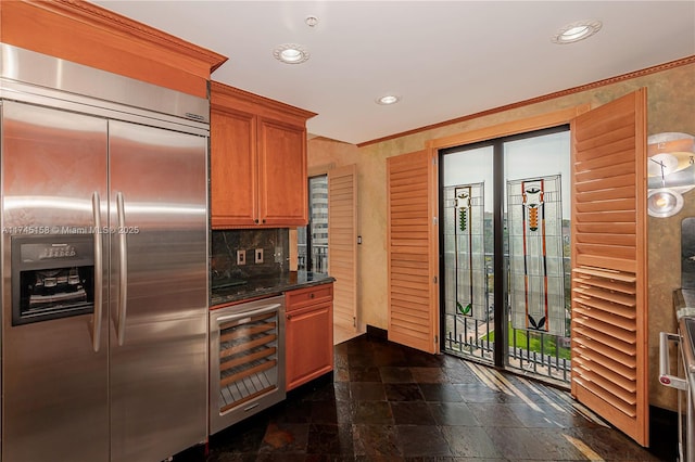 kitchen with built in fridge, wine cooler, brown cabinets, stone finish floor, and dark stone counters