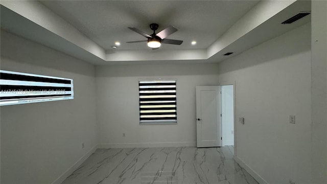 empty room with ceiling fan and a raised ceiling