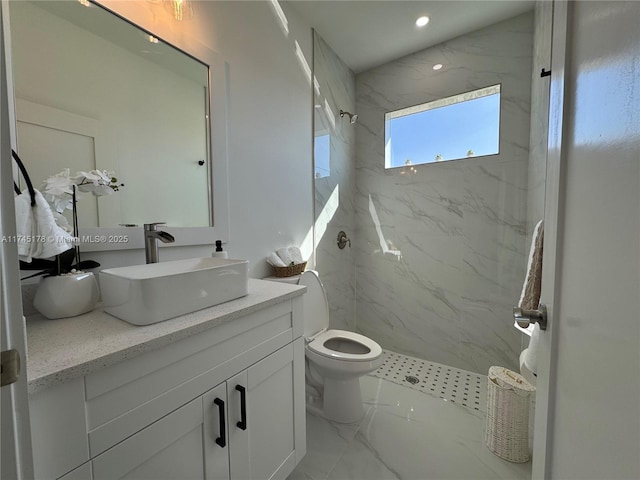 bathroom with a tile shower, vanity, and toilet