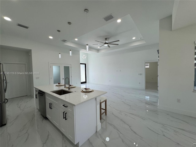 kitchen with sink, appliances with stainless steel finishes, a tray ceiling, an island with sink, and white cabinets