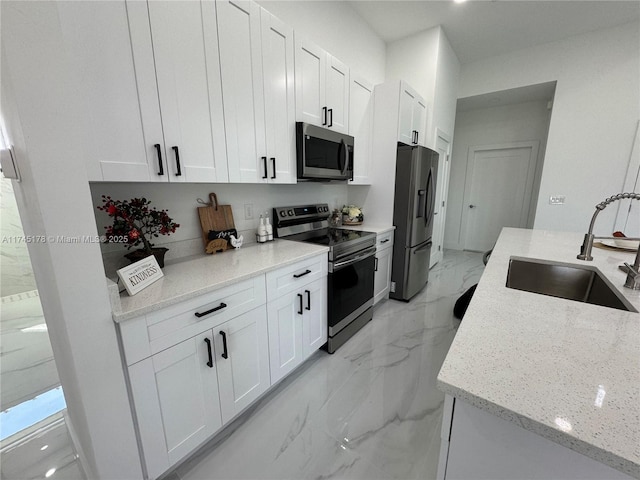 kitchen with stainless steel appliances, light stone countertops, sink, and white cabinets