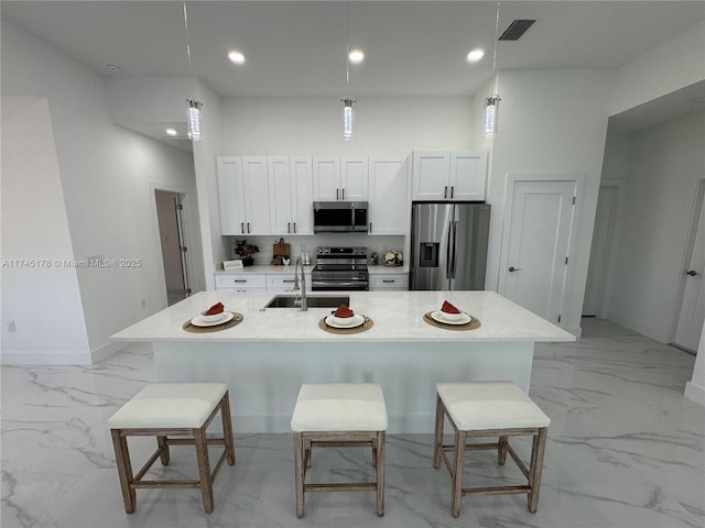 kitchen featuring stainless steel appliances, decorative light fixtures, a breakfast bar, and white cabinets