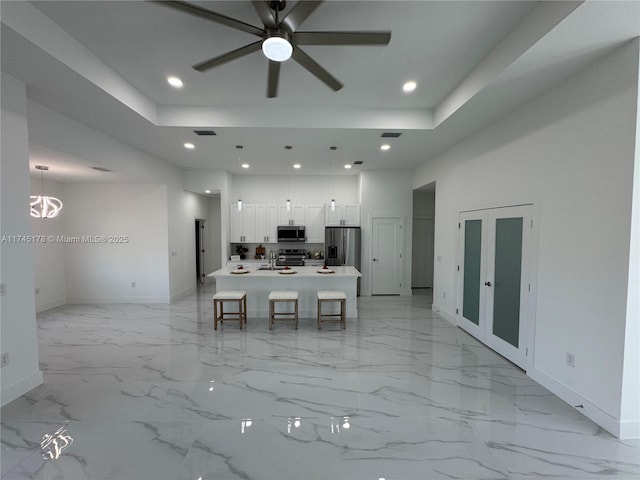 unfurnished dining area featuring sink, ceiling fan with notable chandelier, and a raised ceiling