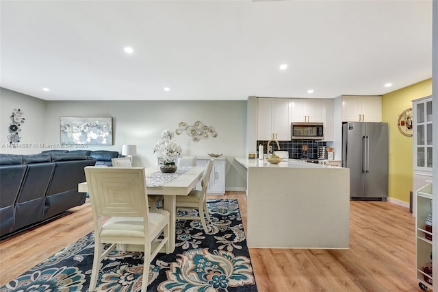 kitchen featuring tasteful backsplash, white cabinetry, a kitchen breakfast bar, stainless steel appliances, and light hardwood / wood-style flooring