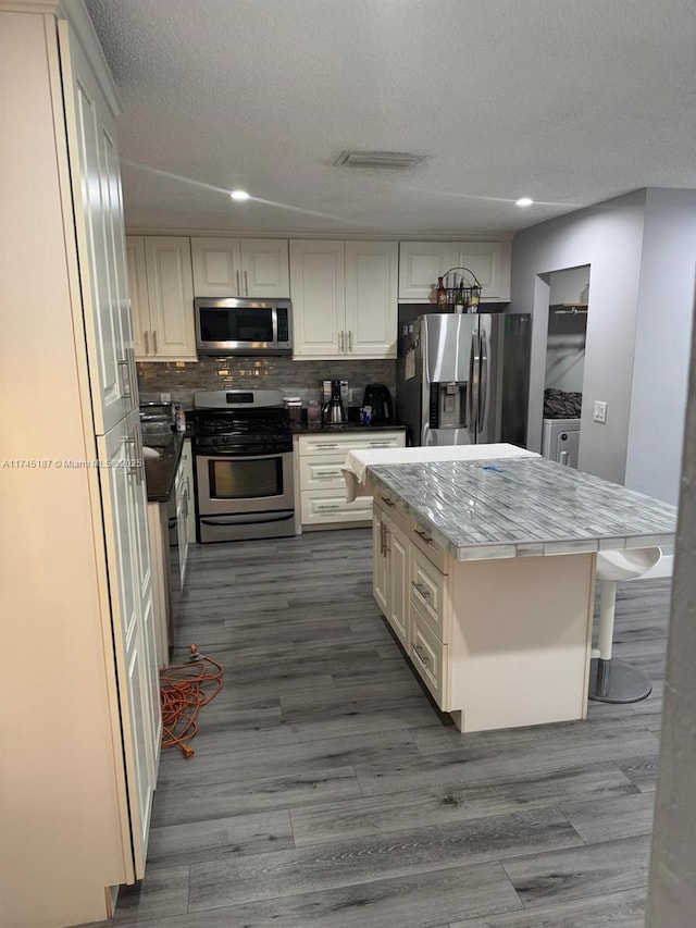 kitchen featuring a center island, a textured ceiling, stainless steel appliances, hardwood / wood-style floors, and backsplash