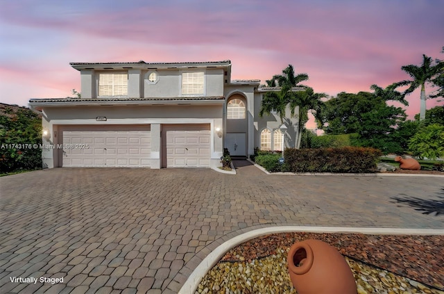 mediterranean / spanish house featuring an attached garage, a tiled roof, decorative driveway, and stucco siding