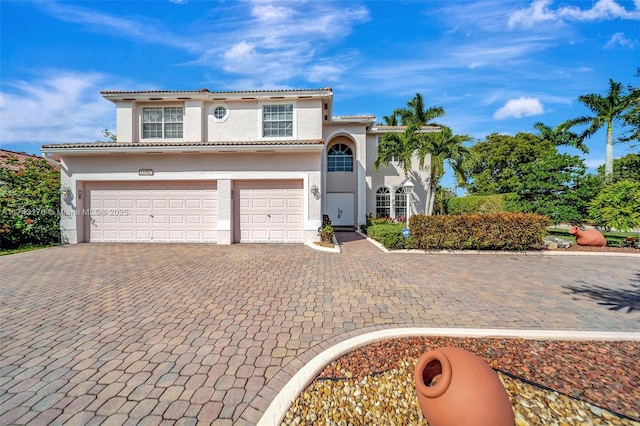 mediterranean / spanish home featuring a garage, a tiled roof, decorative driveway, and stucco siding