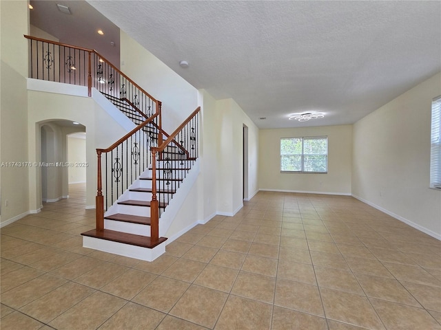 stairway featuring arched walkways, a textured ceiling, tile patterned floors, and baseboards