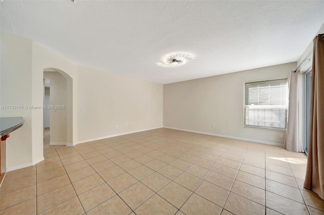 empty room with light tile patterned floors, arched walkways, and a textured ceiling