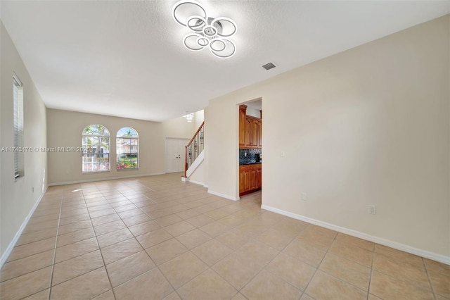 unfurnished living room with light tile patterned flooring, visible vents, stairway, and baseboards