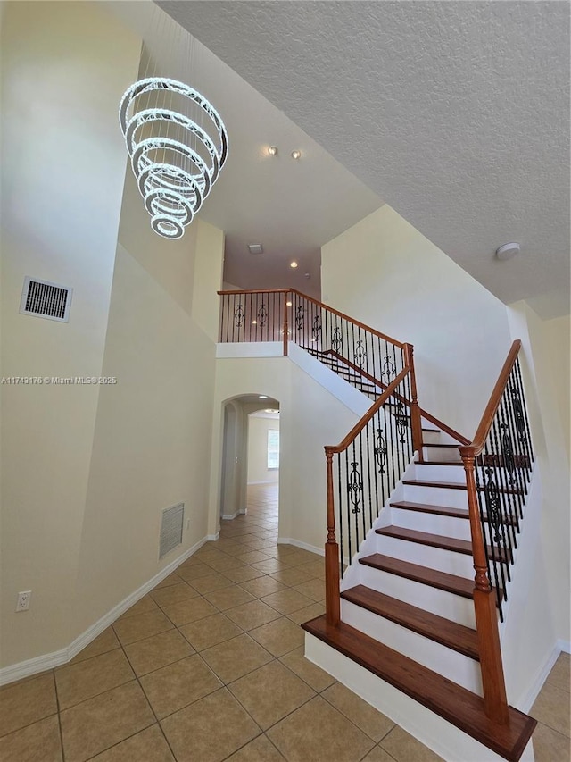 staircase with tile patterned flooring, arched walkways, a chandelier, and visible vents