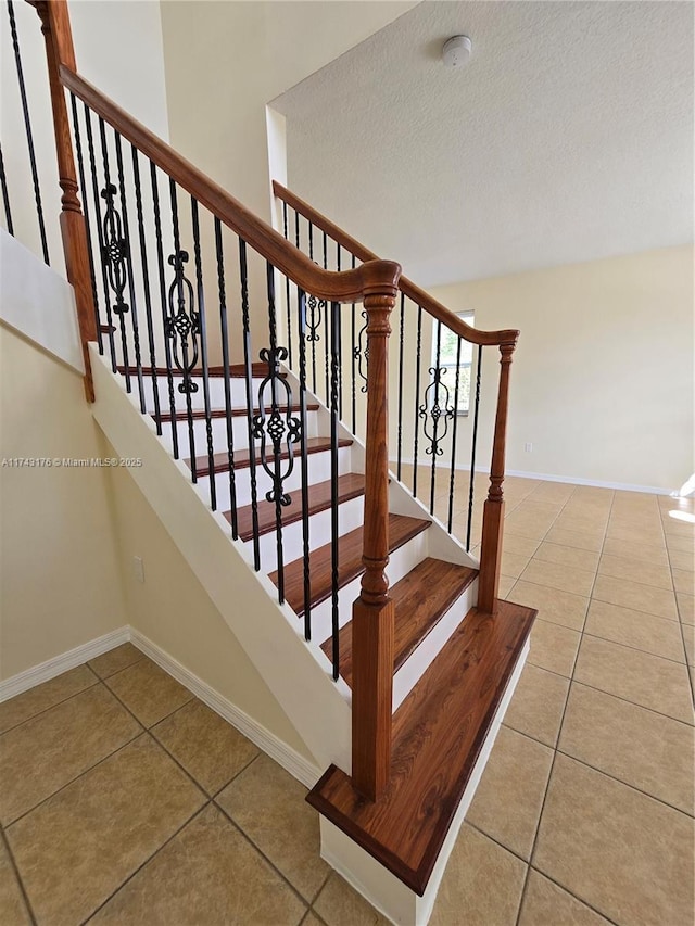 stairs with tile patterned floors, a textured ceiling, and baseboards