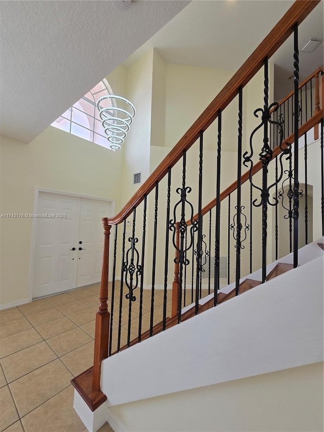 stairs with an inviting chandelier, visible vents, a textured ceiling, baseboards, and tile patterned flooring