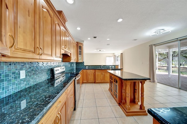 kitchen with electric stove, a sink, glass insert cabinets, tasteful backsplash, and a peninsula