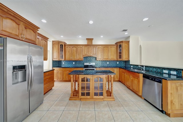 kitchen featuring dark stone countertops, stainless steel appliances, backsplash, and a sink
