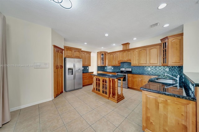 kitchen with dark stone countertops, a sink, visible vents, stainless steel appliances, and backsplash