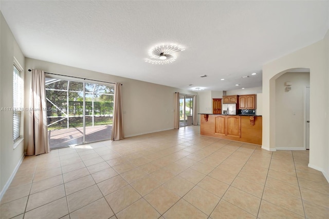 unfurnished living room featuring recessed lighting, light tile patterned floors, a textured ceiling, baseboards, and arched walkways