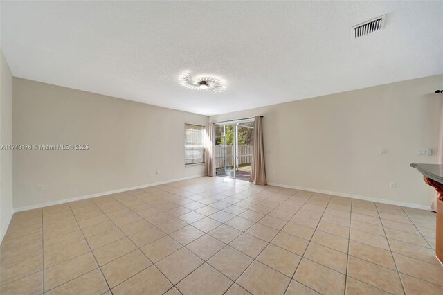 empty room with light tile patterned flooring, visible vents, baseboards, and a textured ceiling
