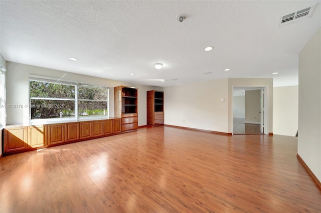unfurnished living room featuring visible vents, light wood-type flooring, a textured ceiling, and recessed lighting