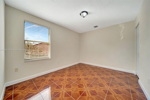 spare room featuring a textured ceiling, visible vents, and baseboards