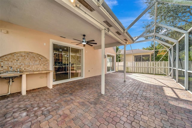 view of patio with a ceiling fan, a sink, glass enclosure, and fence