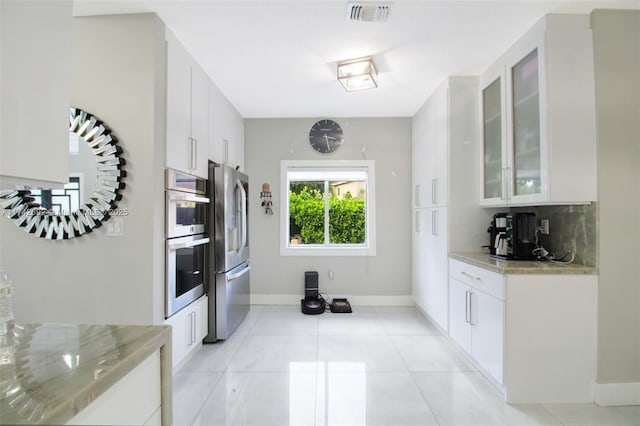 kitchen with tasteful backsplash, light tile patterned floors, appliances with stainless steel finishes, light stone countertops, and white cabinets