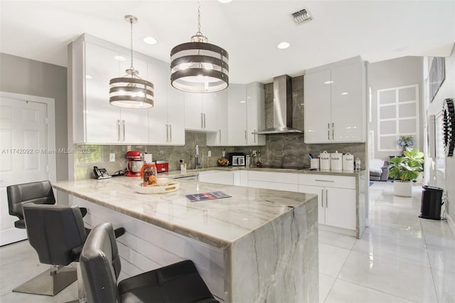 kitchen featuring a breakfast bar area, white cabinets, decorative light fixtures, kitchen peninsula, and wall chimney exhaust hood