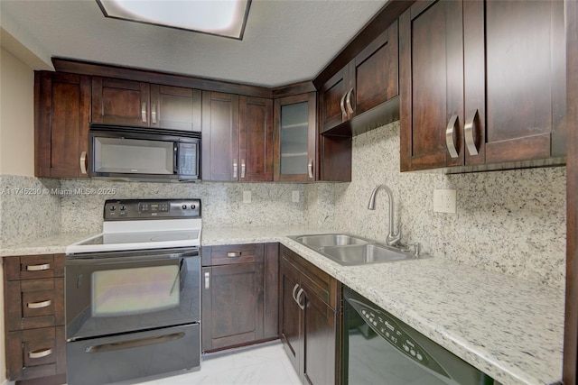 kitchen with dark brown cabinetry, decorative backsplash, glass insert cabinets, black appliances, and a sink