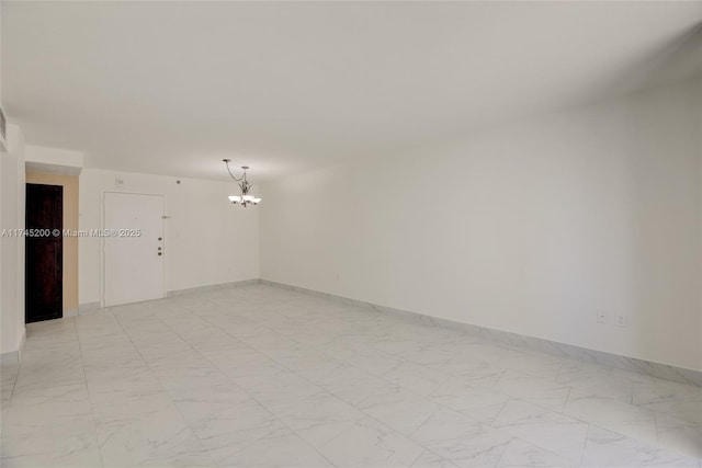 spare room featuring a chandelier, marble finish floor, and baseboards