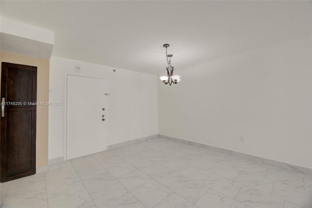 empty room featuring baseboards, marble finish floor, and a notable chandelier