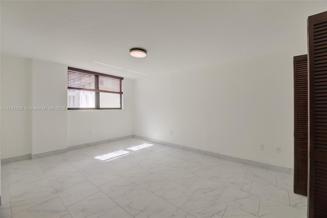 spare room featuring marble finish floor and baseboards